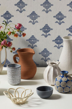 various vases and bowls on a table with wallpaper in the backround