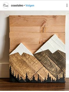 a wood block with mountains and trees painted on the sides, sitting on a wooden floor