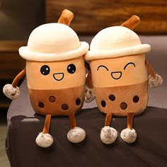 two coffee cups are sitting on a bed with their faces covered by pillows and hats