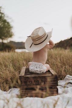 a baby wearing a hat sitting on top of a wooden crate in a field with tall grass