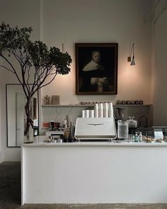 a white counter top sitting under a painting next to a potted plant and tree