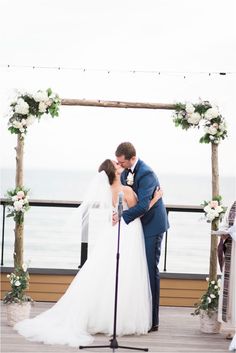 a bride and groom kissing in front of an outdoor wedding ceremony set up on the pier