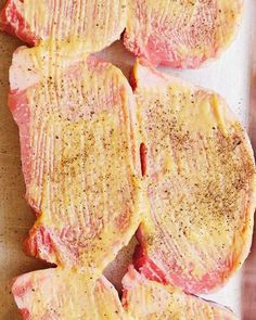 four pieces of raw meat sitting on top of a cutting board with seasoning sprinkled on them