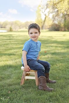 a little boy sitting on top of a wooden chair in the grass with his legs crossed