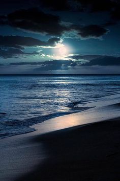 the moon is setting over the ocean with dark clouds and blue water in the foreground