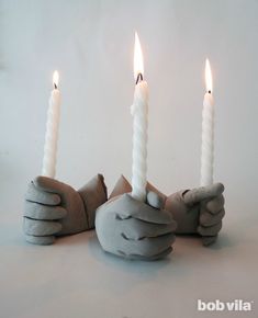 three white candles with hands holding them in front of each other on a white background