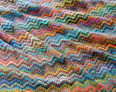 a multicolored crocheted blanket is laying on the ground