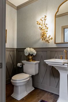 a white toilet sitting next to a sink in a bathroom under a mirror and gold accents