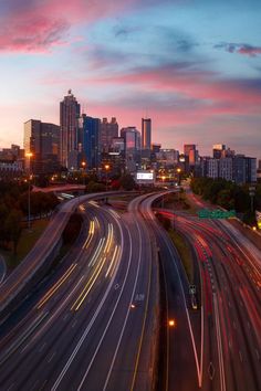 the city skyline is lit up at night with long exposure and light streaks on the road