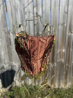 a corset made out of fabric with flowers and leaves on the bottom, sitting in front of a fence