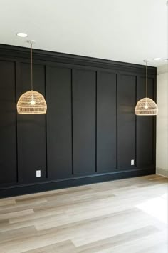 an empty room with black paneling and two pendant lights hanging from the ceiling above it