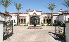 an entrance to a large home with palm trees in the front yard and gated courtyard