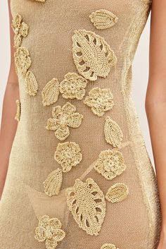 the back of a woman's gold dress with flowers and leaves embroidered on it