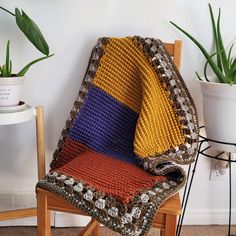 a crocheted blanket sitting on top of a wooden chair next to a potted plant