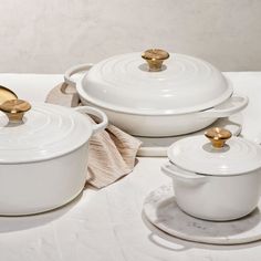 a table topped with white pots and pans covered in gold rimmed dishes next to glasses