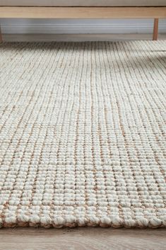 a white rug on the floor with a wooden table in the background and an open window behind it