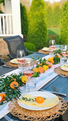 the table is set with plates, glasses and oranges for an outdoor dinner party