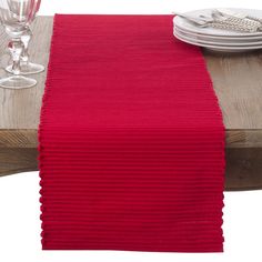 a red table runner on top of a wooden table with wine glasses and silverware