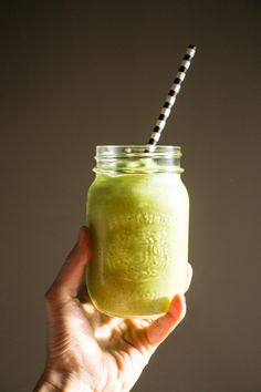 a hand holding a green smoothie in a mason jar