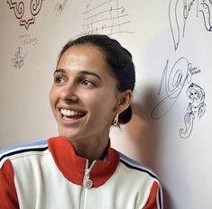 a woman smiling next to a wall with drawings on it