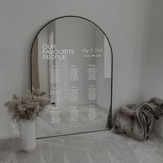 a mirror sitting on top of a floor next to a vase filled with flowers