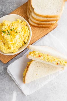 there is a bowl of scrambled eggs next to some slices of bread on a cutting board