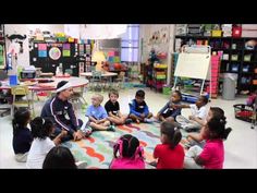 a group of children sitting on the floor in front of a man talking to them