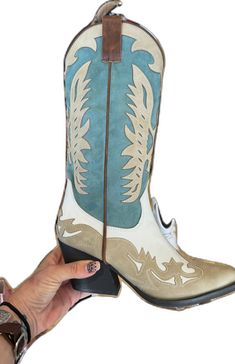 a hand holding up a pair of cowboy boots with blue and white paint on them