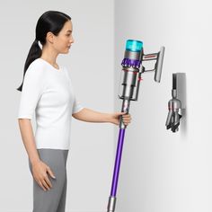 a woman is holding onto the handle of a cordless vacuum cleaner while standing in front of a white wall