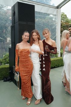 three women standing next to each other in front of a glass wall at an event