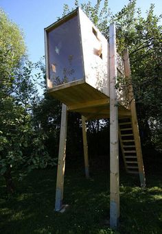 a tall wooden structure sitting on top of a lush green field next to trees and bushes