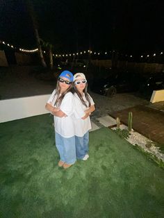 two women standing in the grass at night with their arms around each other, both wearing sunglasses