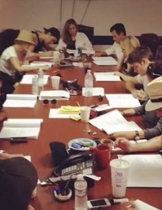 a group of people sitting at a long table with papers and pens in front of them