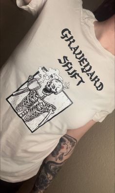 Elevate your style with our exclusive "Graveyard Shift" tee showcasing unique artwork. Stand out from the crowd with Dark Majesty's distinctive apparel, designed for goth and alternative parents, as well as individuals of all backgrounds! Thank you for supporting my small business! 🖤🤘 Fitted T-shirt With Custom Print For Fan Merchandise, White Band Merch Top With Custom Artwork, Cotton Band Merch T-shirt With Custom Artwork, Band Merch Cotton T-shirt With Custom Artwork, Fitted Alternative Style T-shirt With Graphic Print, Unisex Crew Neck T-shirt With Custom Artwork, Cotton Tops With Custom Band Artwork, Custom Artwork Short Sleeve Shirt For Streetwear, Cotton Tops With Custom Artwork For Streetwear