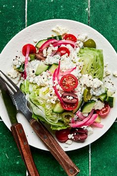 a white plate topped with lettuce, tomatoes and feta cheese next to a knife