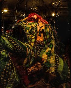 a woman with red hair is dressed in green and black clothing while sitting on the ground