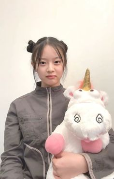 a woman holding a stuffed unicorn with a gold horn on it's head and wearing a gray jacket