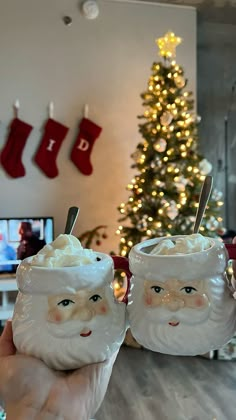 two mugs with whipped cream in front of a christmas tree