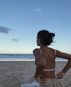 a woman sitting on top of a sandy beach next to the ocean with her back turned