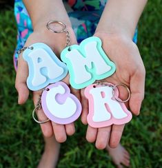 two hands holding three key chains with letters on them