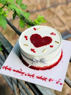 a white cake with red frosting and a heart on top sitting on a table