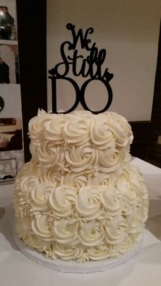 a wedding cake with white frosting and the words we still do on top is sitting on a table