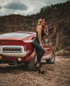 a woman leaning on the hood of a red car