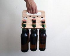 a person is holding three beer bottles in the air with a wooden carrier attached to it