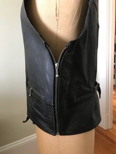 "Black leather hooded vest for either male or female. Imposing look to this leather vest would make a great addition to the heavy metal rocker musician's arsenal of stage wear. Industrial metal zippers and a laced up front closure are the design detail accents on this piece. Wedding attire perhaps for a Goth bridegroom! Hood zips up the back and can be removed as it snaps on or off. Top shoulder zippers and side entrance zippers on either side with a rear buckle to tighten or loosen. Made by 'Ri Rocker Style Fitted Vest For Streetwear, Fitted Leather Biker Jacket For Alternative Fashion, Gothic Black Leather Biker Jacket, Fitted Black Rocker Vest, Black Fitted Rocker Vest, Winter Leather Vest For Biker Events, Fitted Leather Jacket For Stylish Wear, Leather Biker Jacket For Cosplay, Biker Leather Jacket For Cosplay