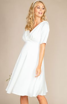 The Zoey maternity wedding dress is simple, refined and elegant.Heavyweight sheen satin has a gentle stretch making it sumptuous and comfortable to wear all day (and night) long. A cross over neckline features dramatic pleats from shoulder to waist. Elbow length sleeves and a knee length skirt create a fun and flirty finish to this sweet bridal style you will love. Add a touch of sparkle with one of our many decorative bridal sashes or choose a beautiful headband for playful glamour. Cross-over Elegant White Maternity Dress, Elegant White Maternity Wedding Dress, Elegant White Maternity Bridesmaid Dress, Elegant Maternity Dress With Empire Waist, Elegant Maternity Maxi Dress With Empire Waist, Fitted Empire Waist Maternity Dress For Wedding, Elegant Maternity Dress With Fitted Bodice, Elegant Maternity Maxi Dress, Elegant White Maternity Dress For Bridal Shower