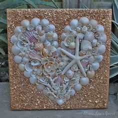 a heart made out of shells and seashells is displayed on a wooden board