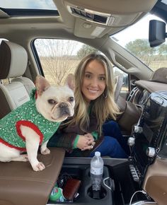 a woman sitting in the back seat of a car with her dog wearing a sweater