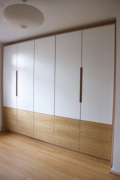 an empty room with wooden floors and white cabinets on the wall, in front of a window