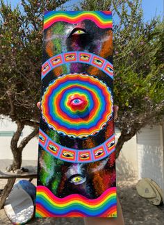 a person holding up a colorful piece of art in front of some trees and bushes